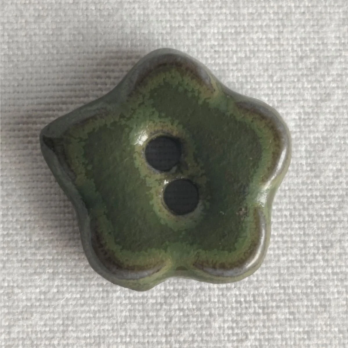 Hand-glazed green ceramic flower button on woven linen